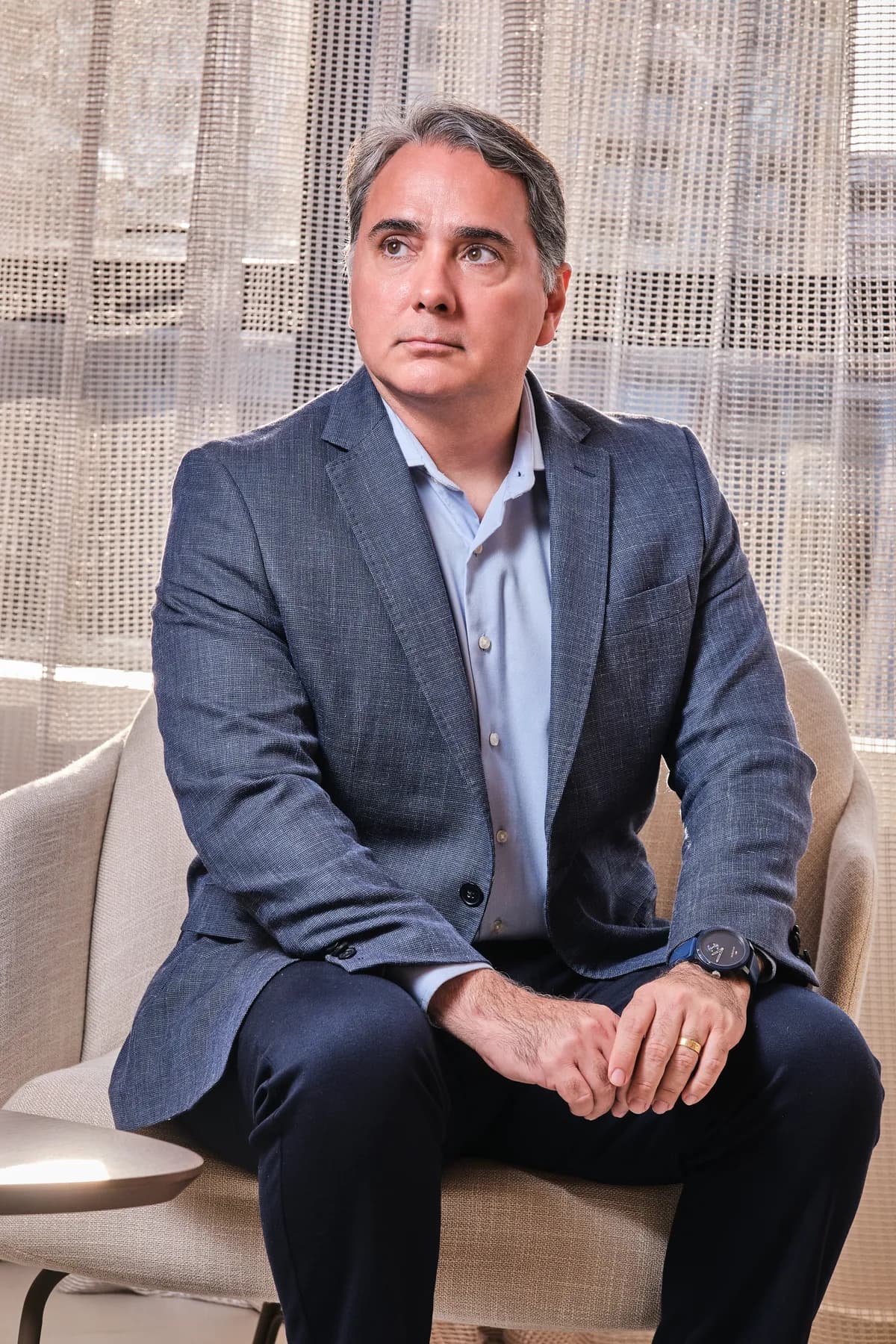 Dr. João Marcelo Lyra sentado numa poltrona da Logos Vision, com as mãos entrelaçadas e o olhar para o lado
