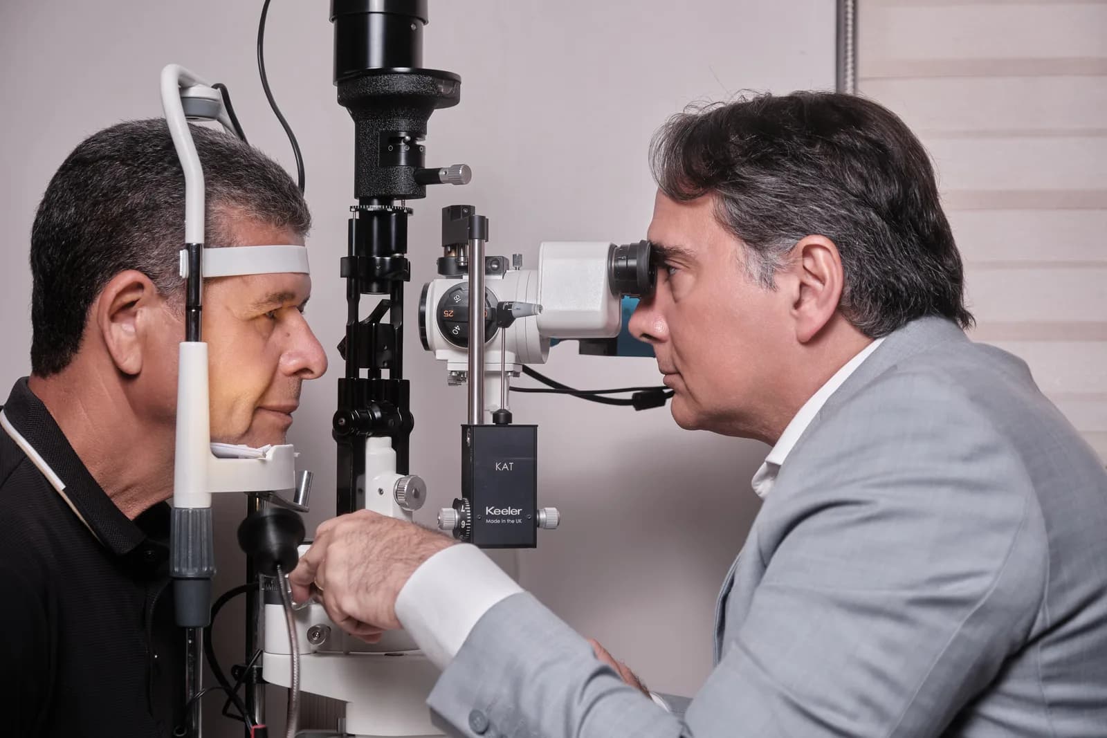 Dr. João Marcelo Lyra, de perfil, examinando um paciente na lâmpada de fenda